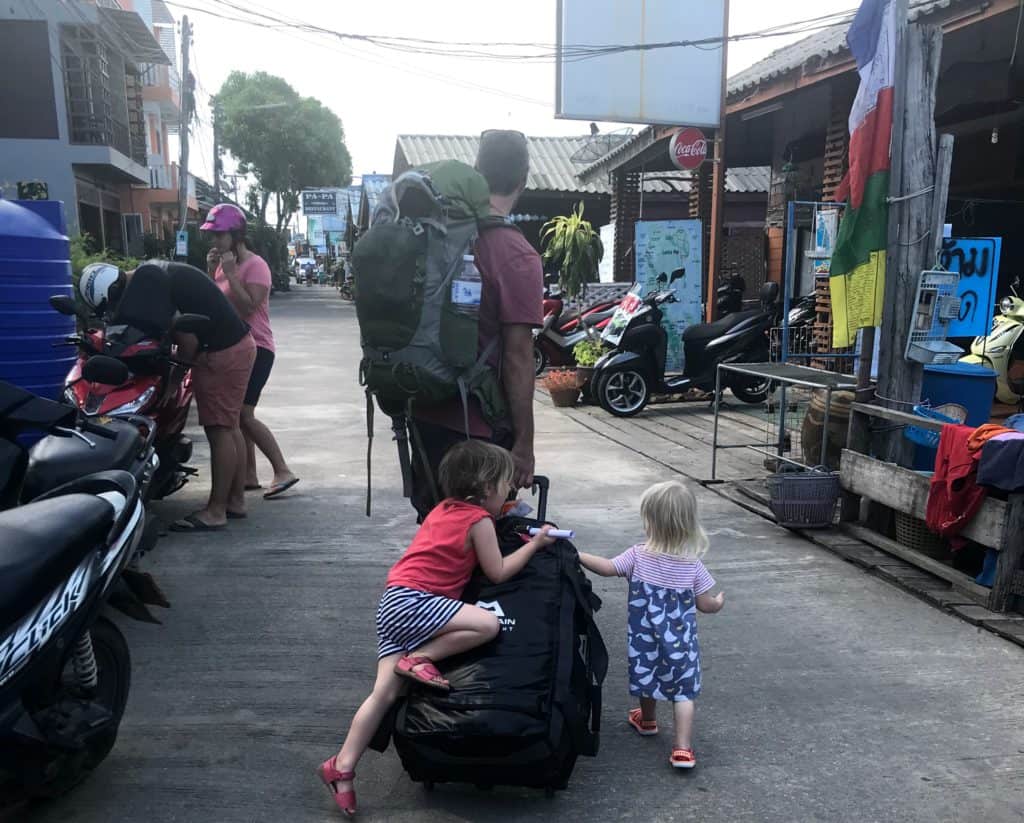 walking along the street in Ko Lanta Thailand with a baby and toddler climbing on to wheeled bag