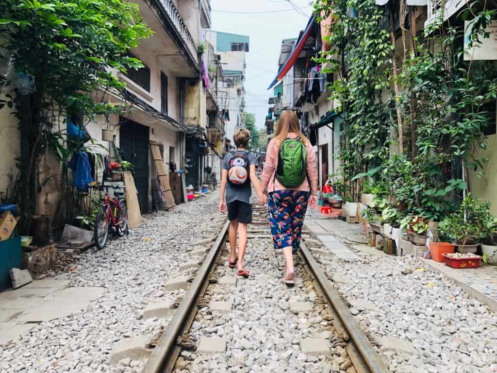 woman and boy walking along train tracks between buildings in Hanoi