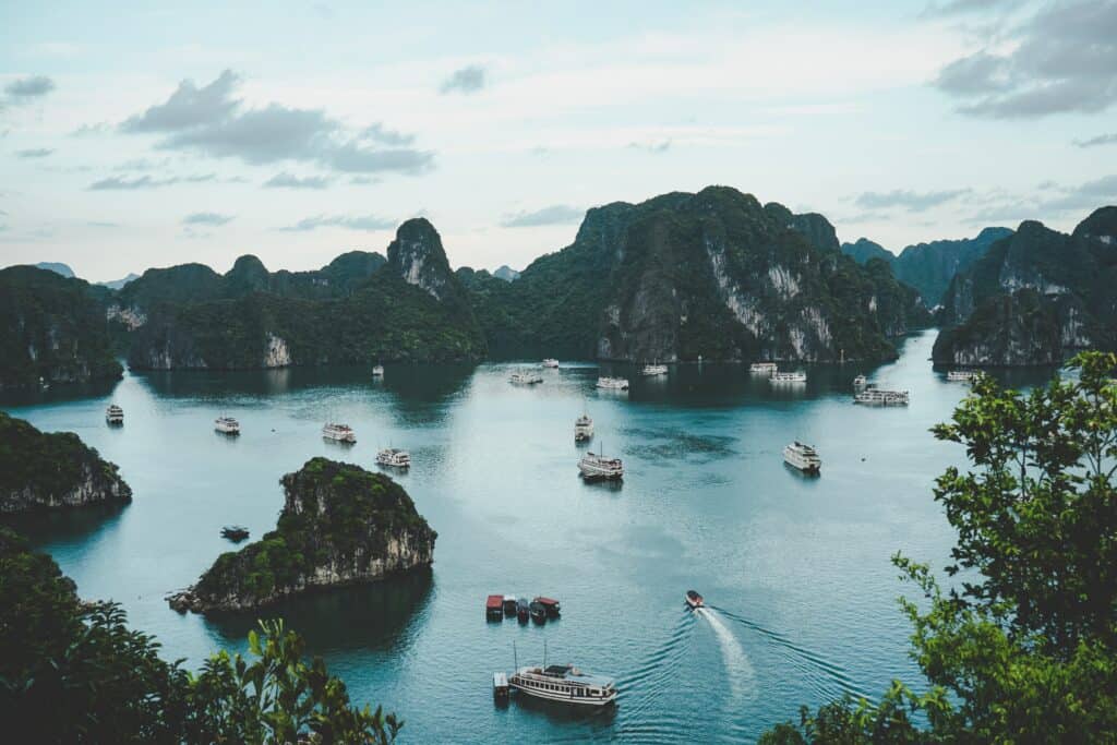 View across water and islands in Halong bay with boats in the water, visited on a Vietnam 10 day itinerary