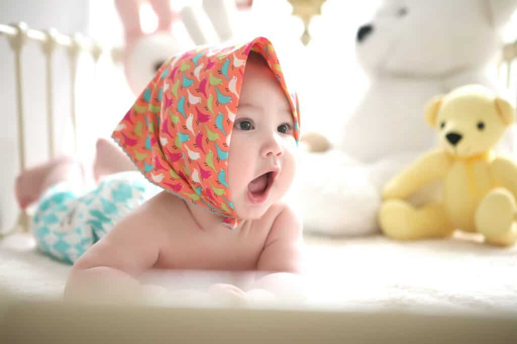 baby with head scarf awake on bed
