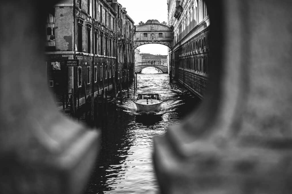 Black and white image of a speedboat infornt of bridges on a canal in Venice
