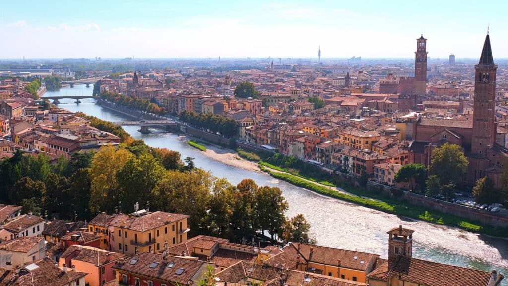Verona skyline of red tiled roofs and church towers split. A river runs through.
