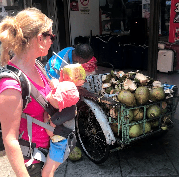 Woman in Penang with a baby in a carrier. drinking coconut milk