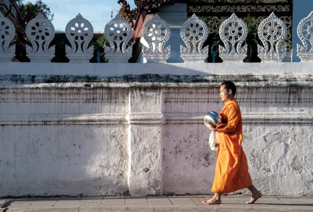Monk in orange robe wlking infornt of white wall - Chiang Mai itinerary