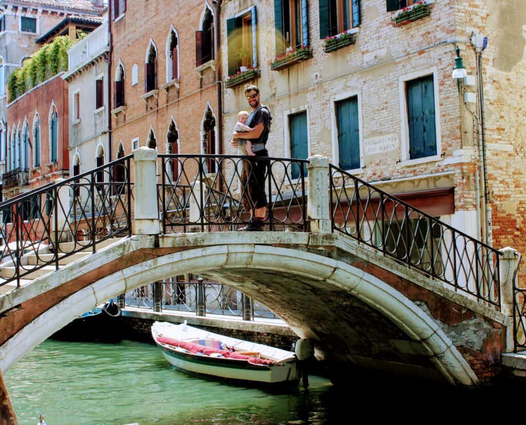 Man in Venice with a baby in a carrier stood on a bridge