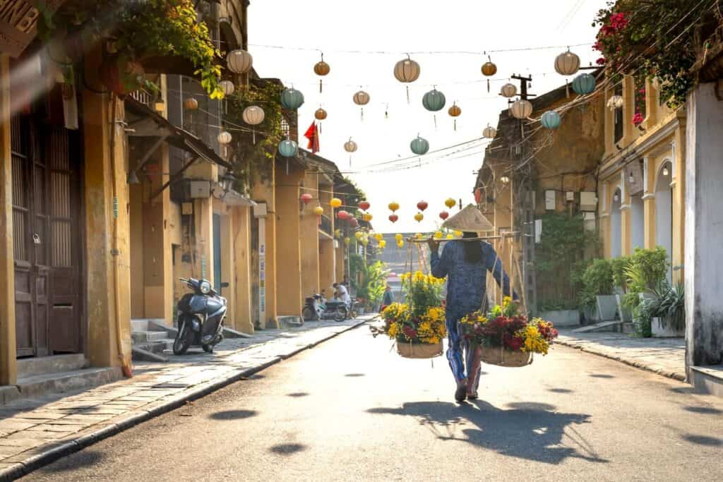 A woman carries baskets of flowers on one of the streets in this Hoi An 3 day itinerary